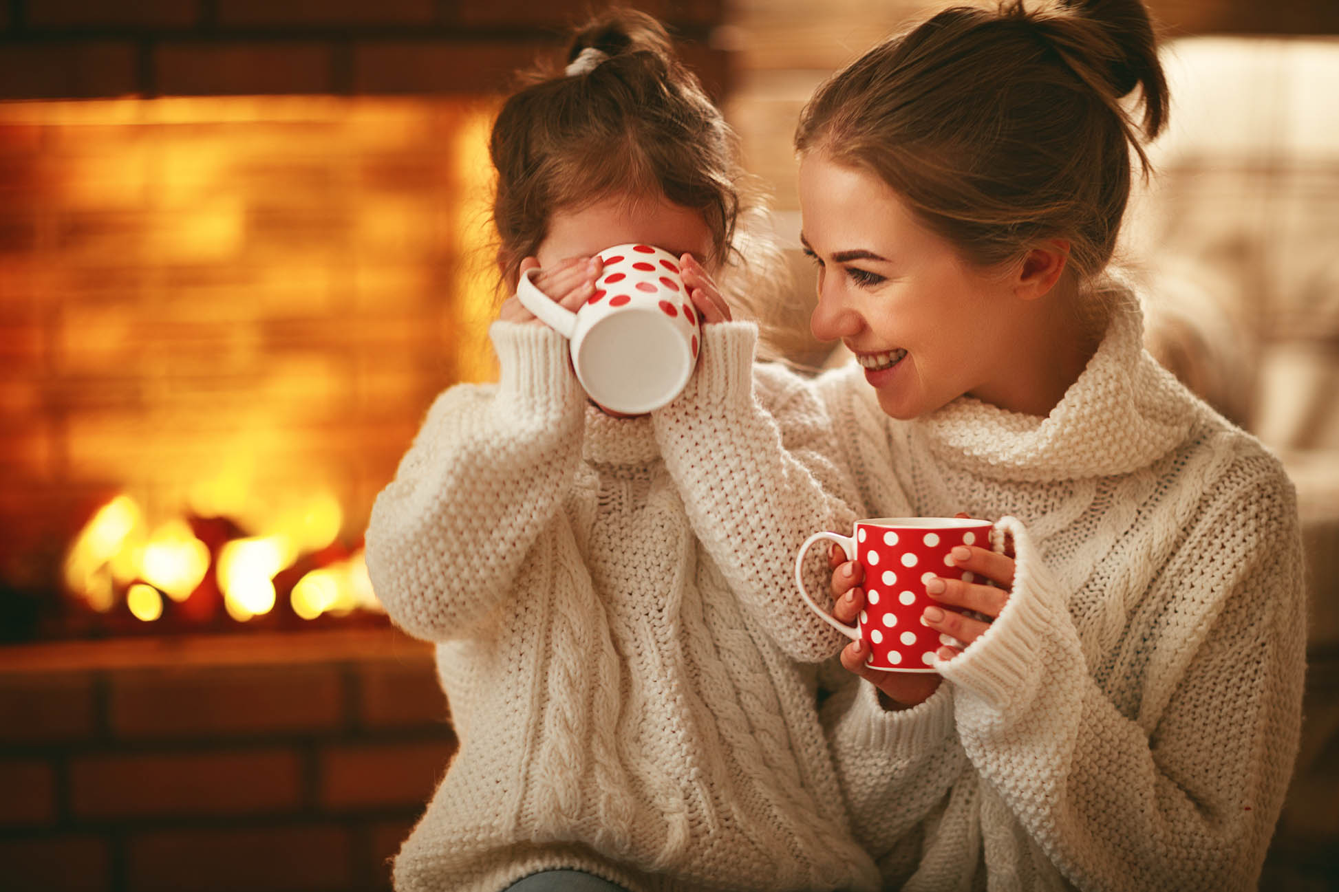Mother and Daughter Wearing Sweaters and Drinking Hot Chocolate in Front of Fireplace